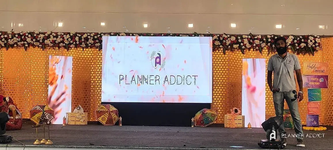 Stage with an LED wall showing the PlannerAddict logo, flanked by flower garlands