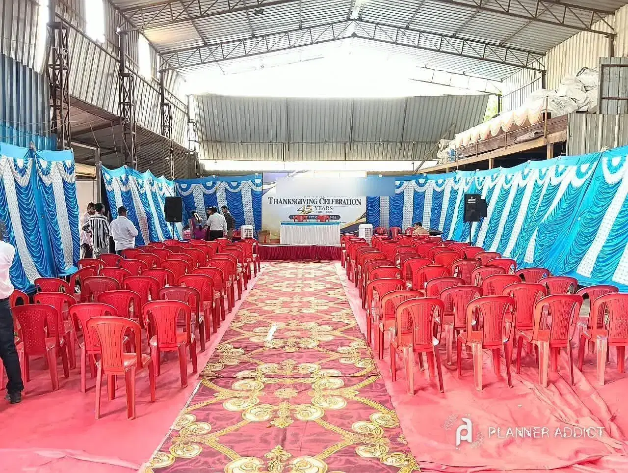 Rows of chairs on a carpeted aisle facing a stage, with blue and white drapes