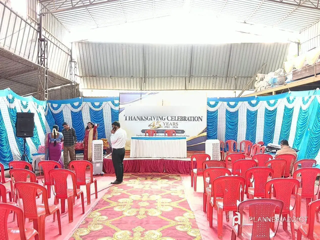 Company celebration in a large shed: stage, backdrop, blue and white drapes and rows of chairs