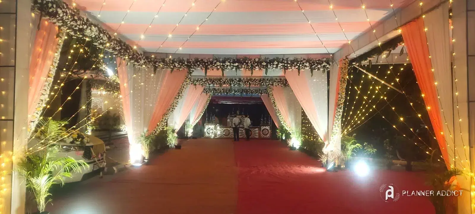 Walkway of peach drapes and fairy lights over a red carpet