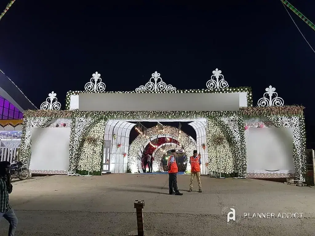 White flower gate at night opening onto a tunnel of lit arches