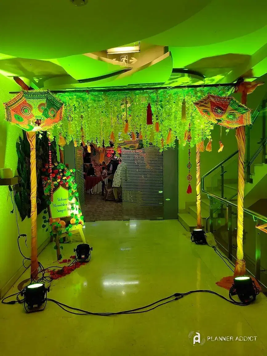 Entrance with a flower-string canopy and umbrellas, lit green