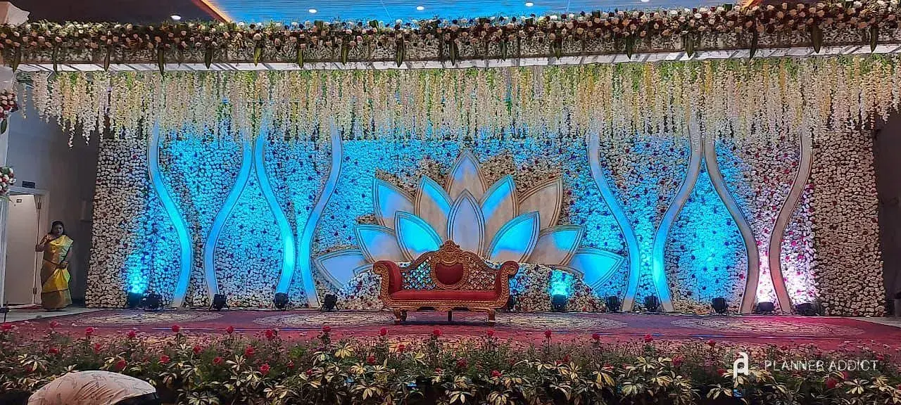 Stage with a blue-lit lotus backdrop and a white flower wall under hanging wisteria