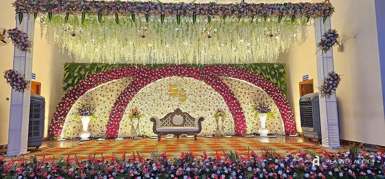 Reception stage with crimson and white flower arcs, a carved sofa and a flower-lined edge