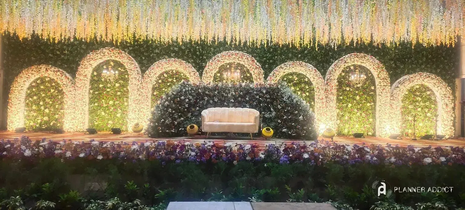 Stage with a row of warmly lit flower arches and a white sofa