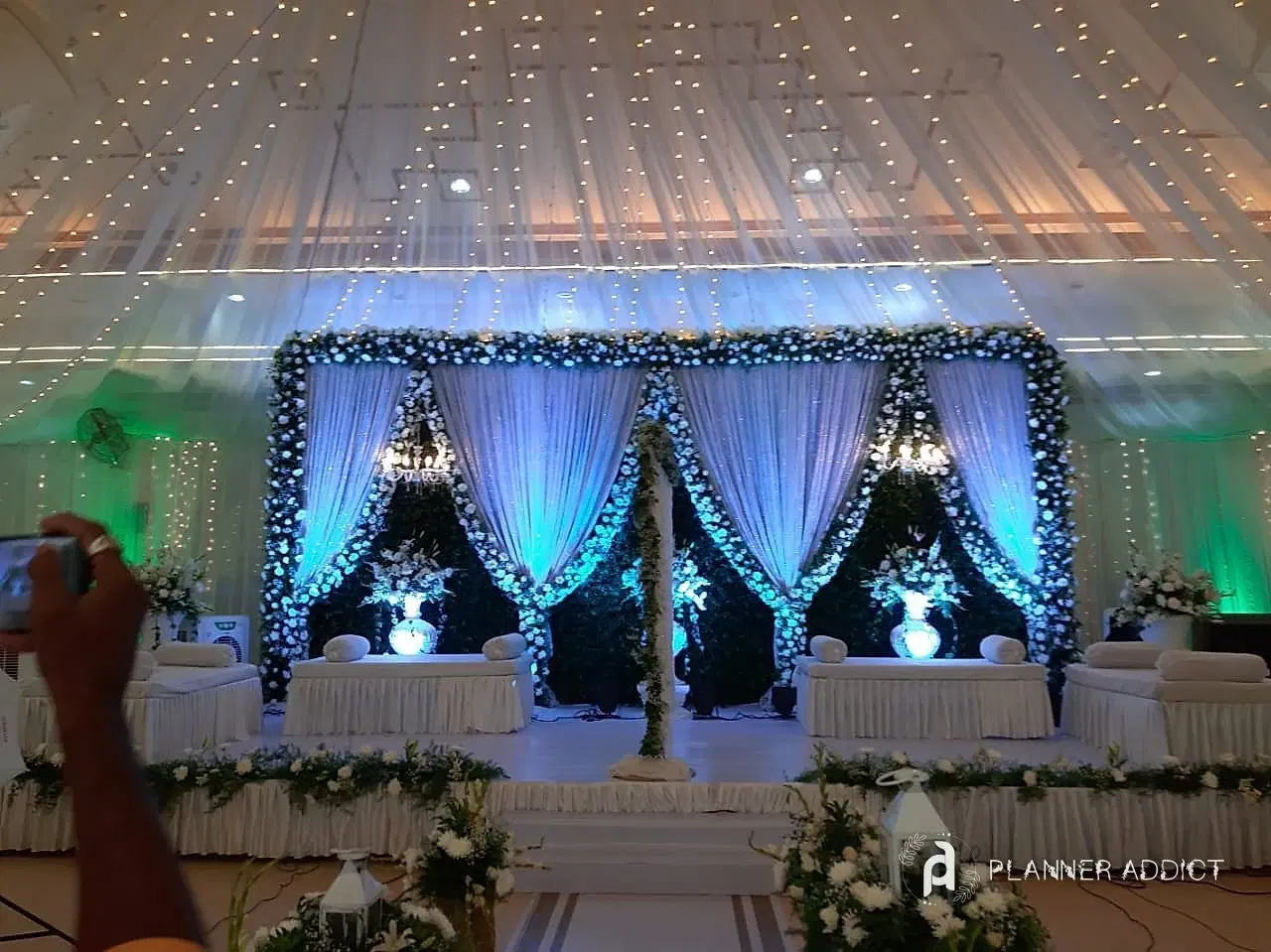 Reception stage with white drapes, green garlands, chandeliers and white sofas