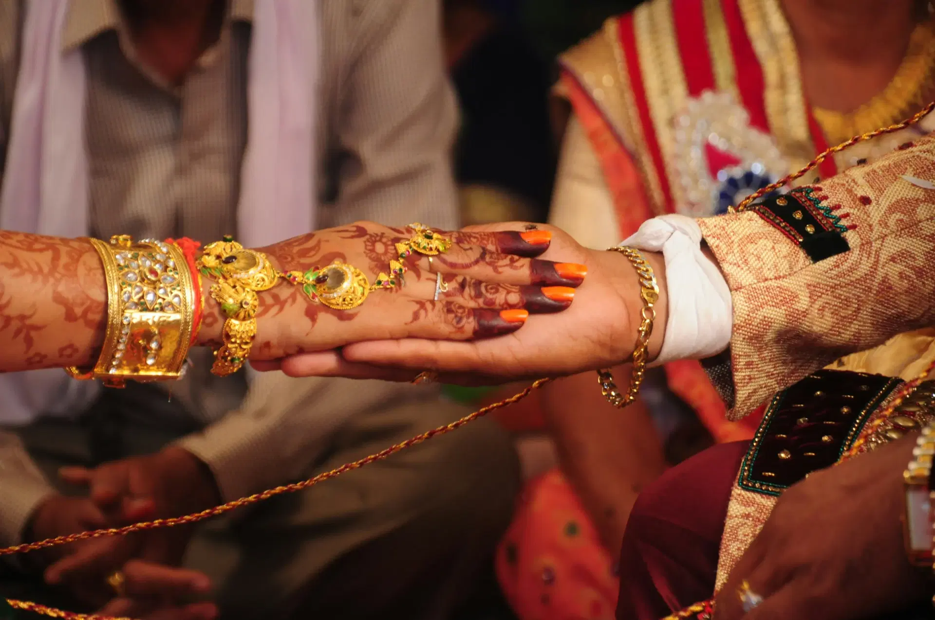 A bride's hennaed hand with gold jewellery placed in the groom's hand during the wedding ritual