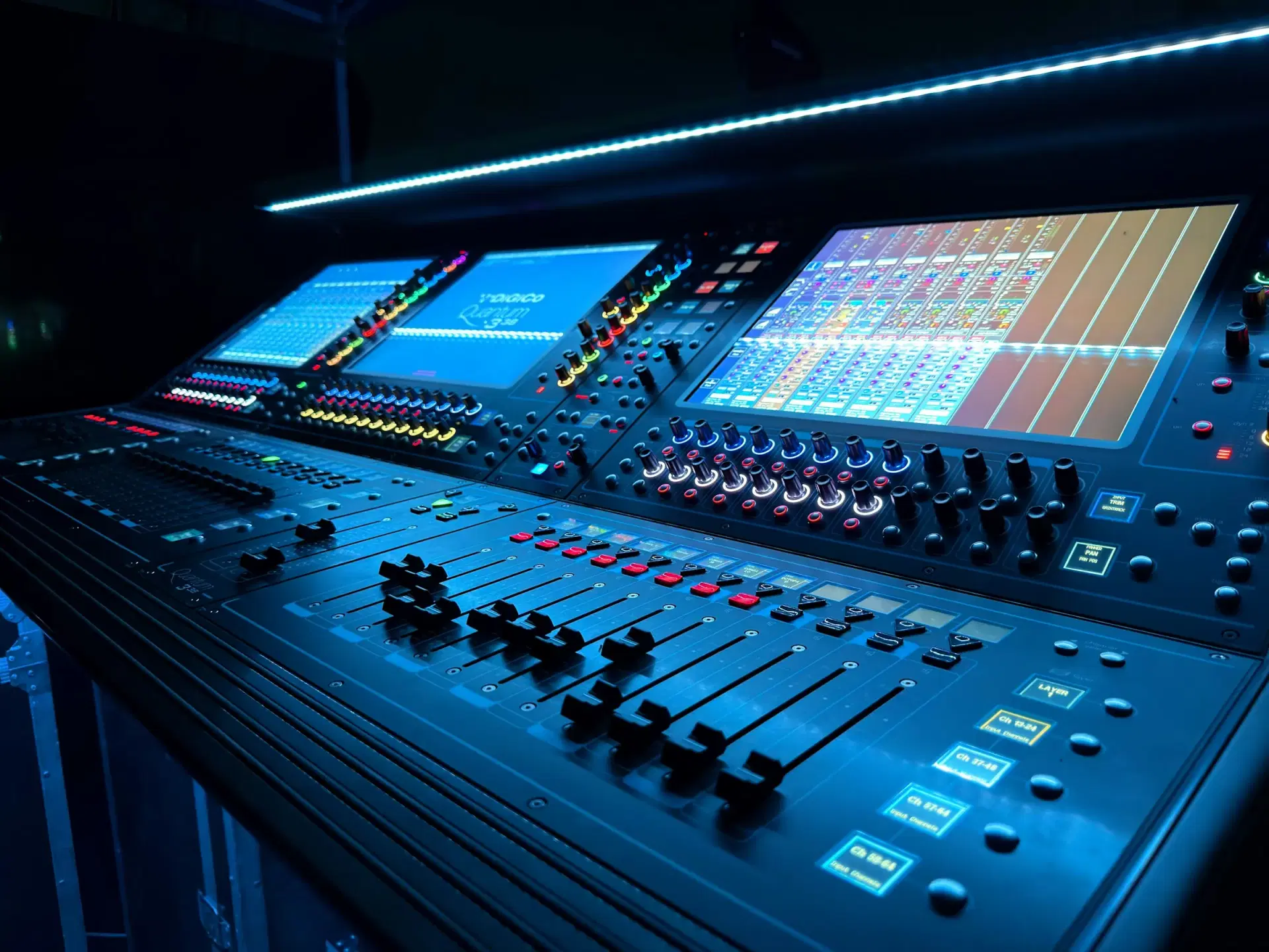 Digital audio mixing console with screens and faders, lit blue
