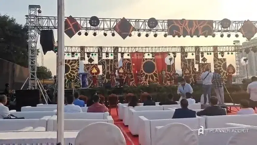 Dancers on a large outdoor truss stage with lights and decorated panels, guests on white sofas in front