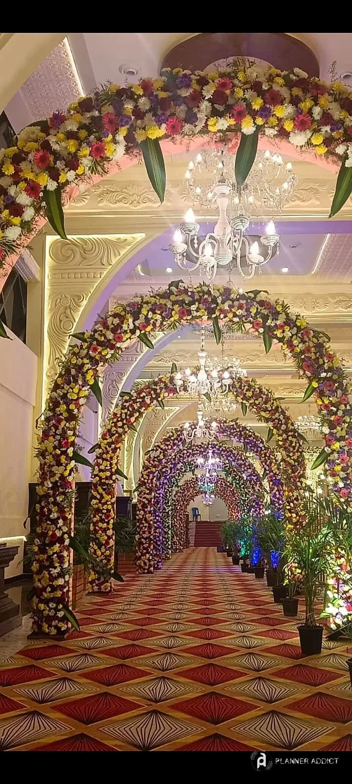 Tunnel of flower arches with chandeliers along a patterned carpet