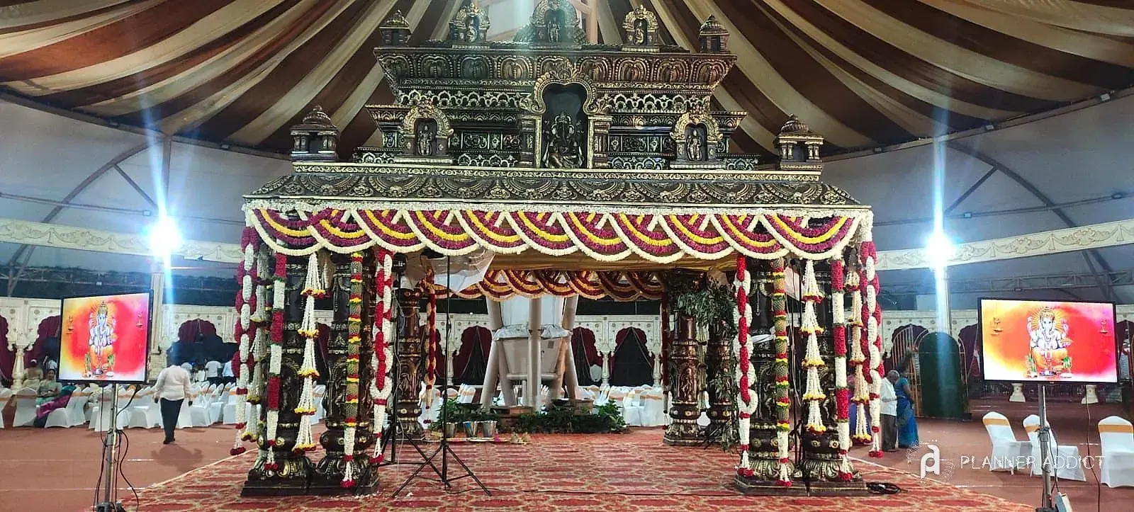 Temple-style mantapa with marigold garlands inside a striped tent