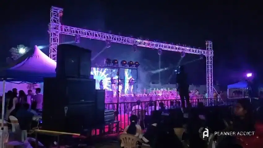 Stacked speakers beside a lit truss stage at a night concert, with the crowd in front