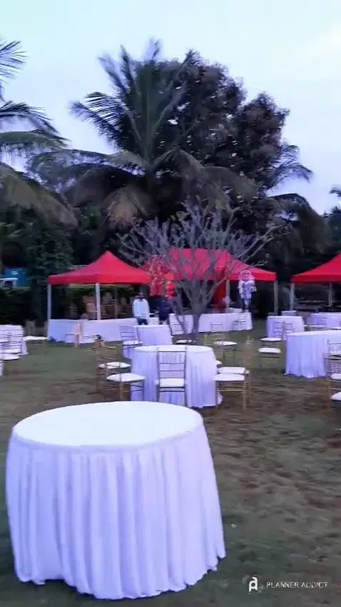 Lawn with round tables, chairs and red canopy tents set up for an evening dinner