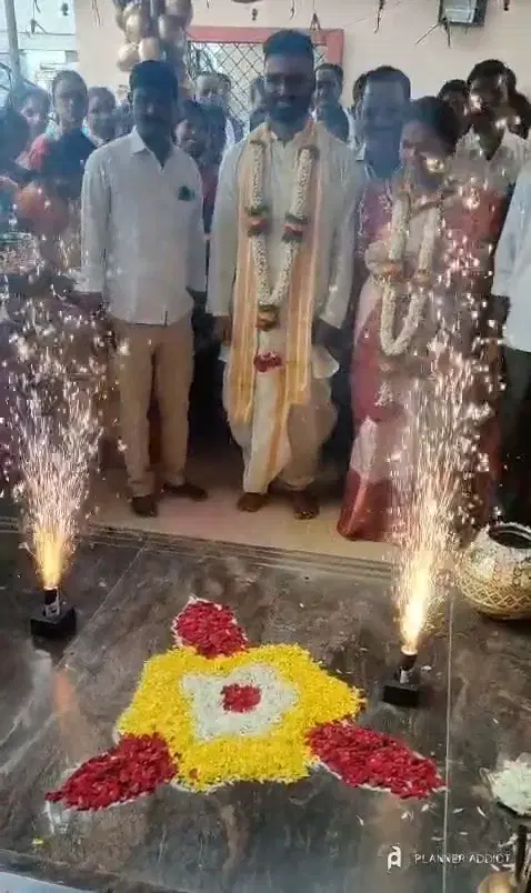 A couple walking in between cold fireworks, past a flower-petal rangoli