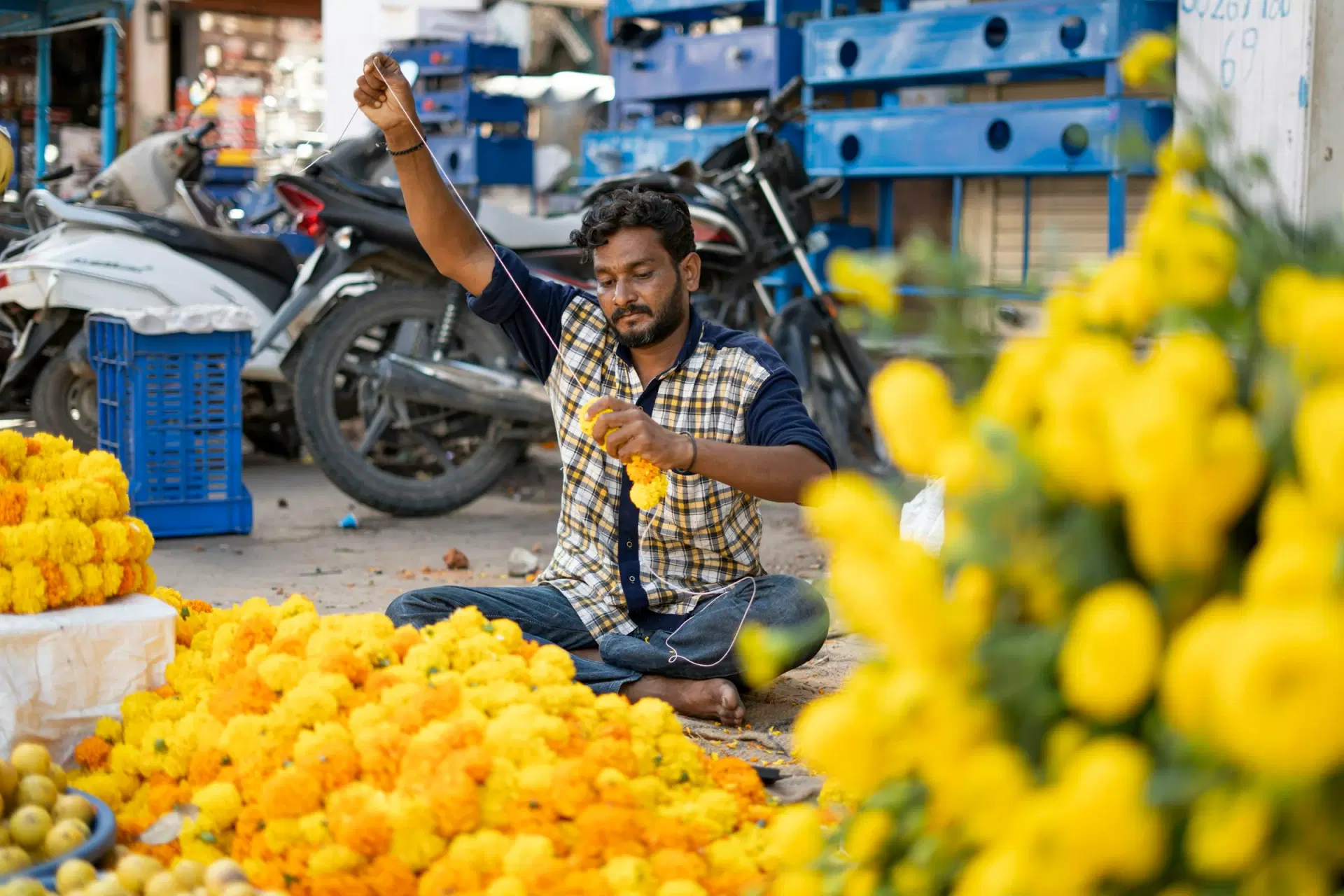 A man stringing yellow marigolds into a garland at a street flower stall