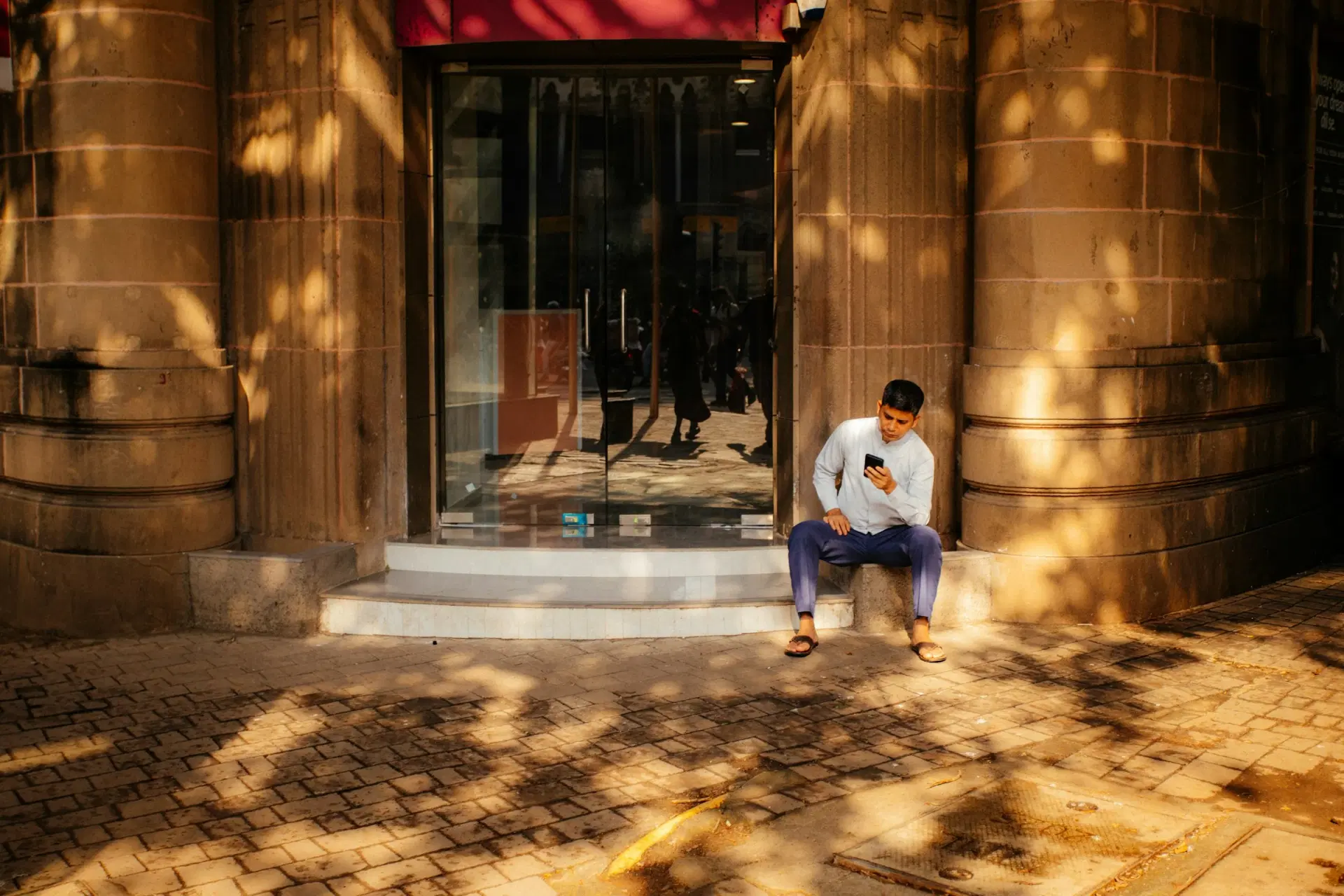 Man sitting on a stone step, using his phone in warm evening light